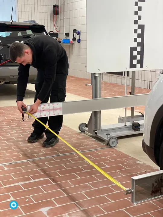 Technicien mesurant au ruban la distance entre le véhicule et le panneau de calibrage ADAS